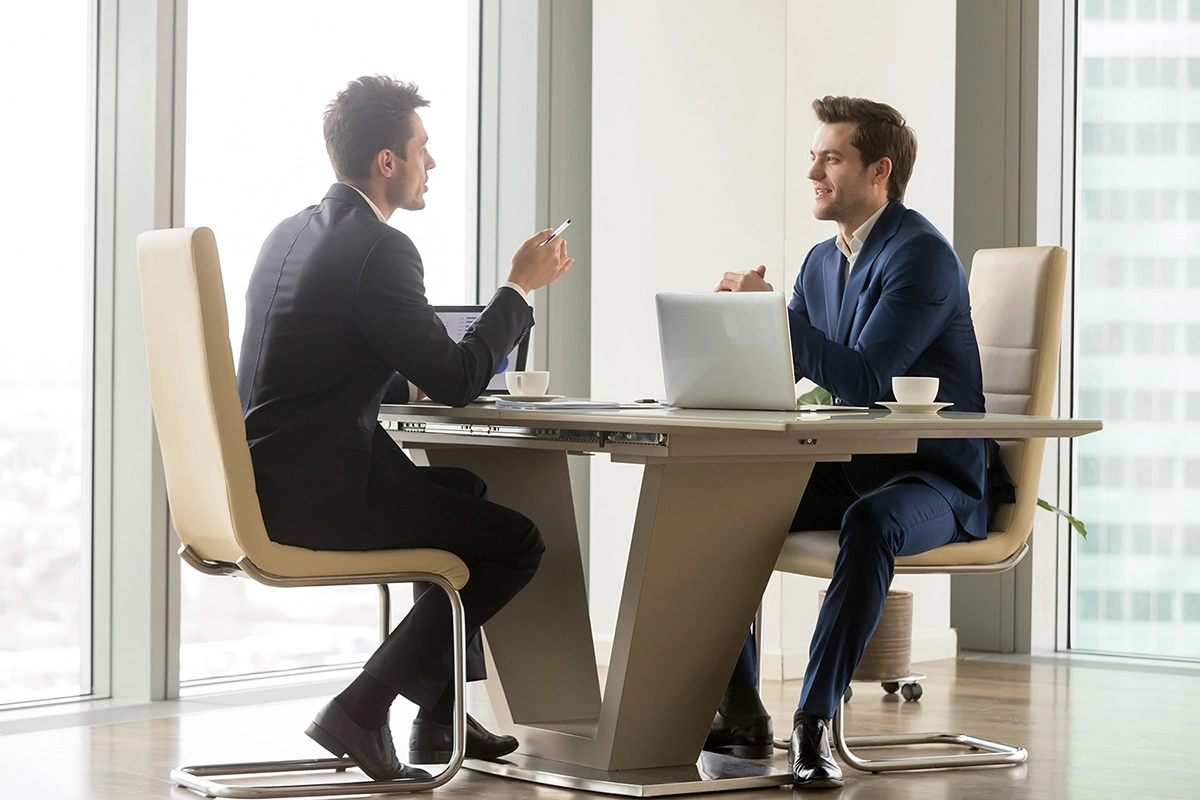 two businessmen discussing work at a modern office table with laptops